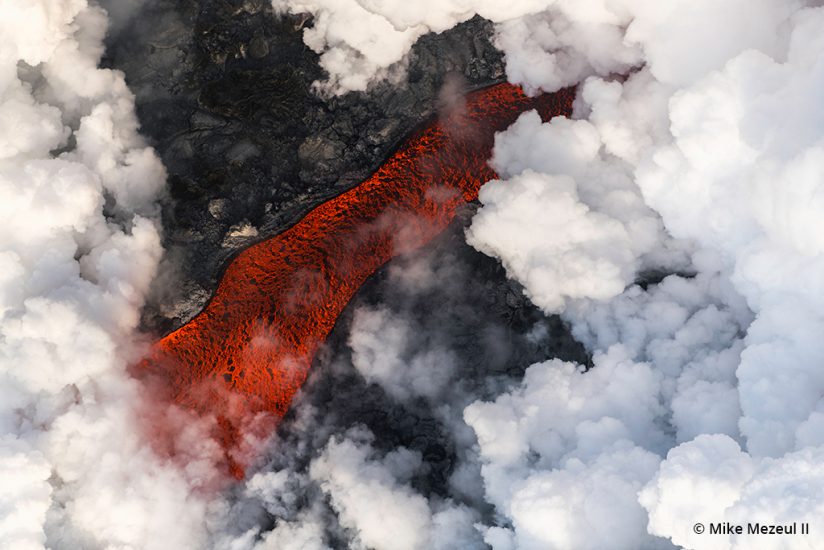 A clearing of steam clouds reveals a river of lava