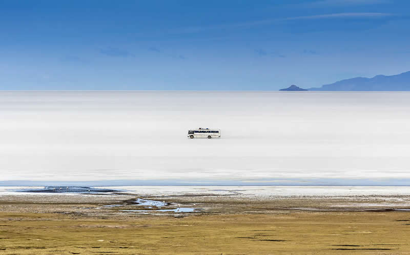 2026 Memorial Maria Luisa Awards: Best Mountain & Nature Photos Revealed 46 A small bus driving across the vast white Uyuni Salt Flats in Bolivia with distant mountains on the horizon.