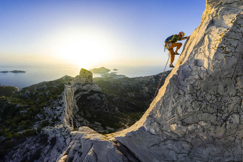 2026 Memorial Maria Luisa Awards: Best Mountain & Nature Photos Revealed 41 A climber scaling a steep rocky ridge above a coastal landscape at sunrise, with ocean and islands visible in the background.