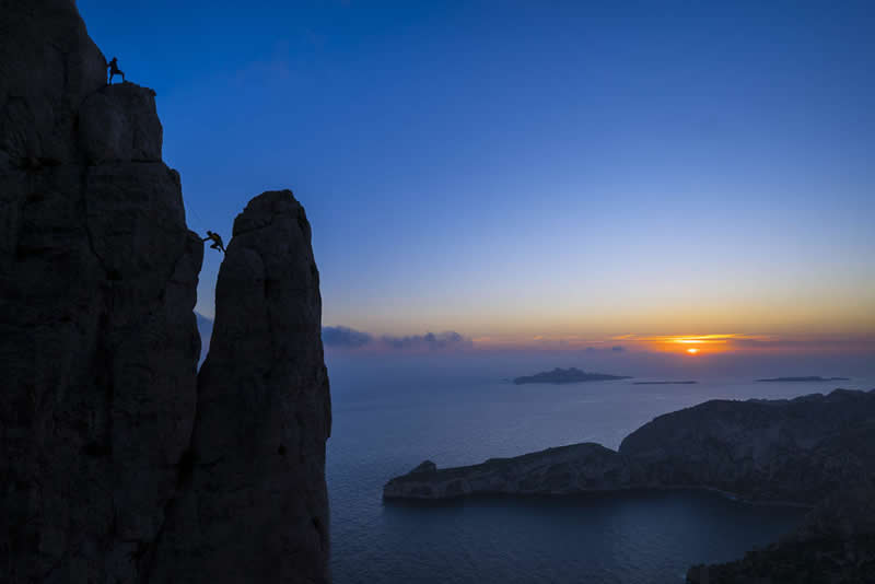 2026 Memorial Maria Luisa Awards: Best Mountain & Nature Photos Revealed 42 Silhouetted climbers on tall sea cliffs at sunset overlooking the ocean and distant islands under a colorful sky.