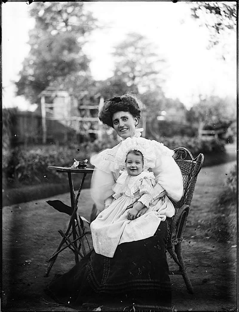 An old-time picture where people are smiling. A mother and her baby smiling for the camera in the early 1900s.