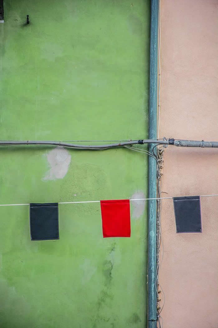 A minimalist scene of a green and beige wall divided by pipes, with three square cloths hanging on a line—two dark and one bright red—creating a striking contrast and geometric balance.