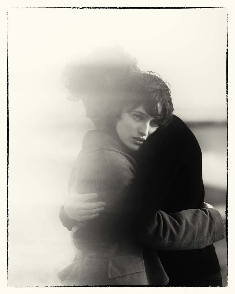 Black and white portrait of two people embracing, with one person looking toward the camera while partially obscured by a soft, hazy overlay, creating an emotional and nostalgic mood.