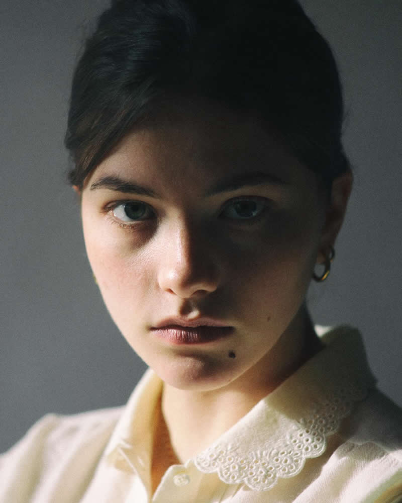 Close-up portrait of a young woman with soft natural light falling across half of her face, creating a dramatic contrast and an intimate, contemplative expression.