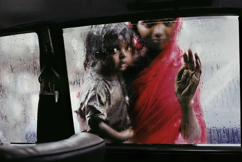 A Mother and Child ask for alms through a taxi Window during the monsoon, Bombay, India by Steve McCurry - Iconic Color Photos by Legendary Photographers