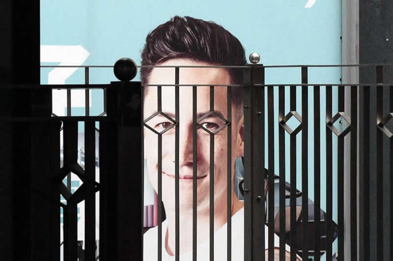 The Art of Perfect Timing: 31 Stunning Street Photos Taken at Exactly the Right Moment 61 Street photograph of a large billboard portrait partially obscured by a decorative metal fence, with the fence bars aligning across the subject’s face to create a striking geometric composition.