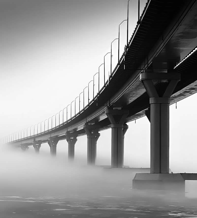The Mobile Revolution: What the Winners of 35AWARDS Tell Us About the Future of Phone Cameras 44 A long bridge curves gracefully across a fog-covered body of water in a black-and-white scene. Repeating support columns and railings create strong leading lines, while dense mist obscures the distance, adding atmosphere, depth, and a sense of mystery.