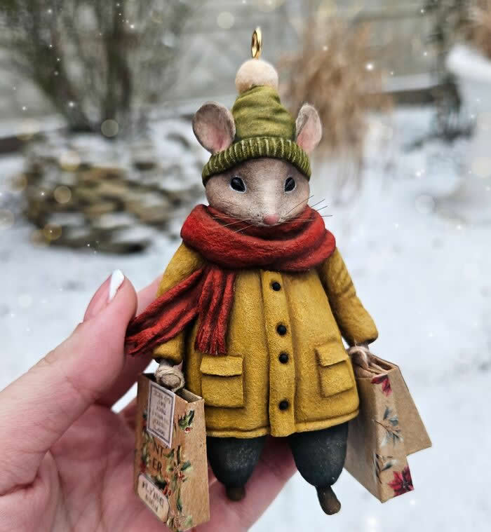 Miniature World: 33 Cotton Wool Sculptures by Katya Celebrating the Magic of Handmade Craft 40 A handcrafted miniature mouse ornament made from cotton wool wears a mustard-yellow coat, green knit hat, and deep red scarf while holding tiny shopping bags against a softly blurred snowy background.