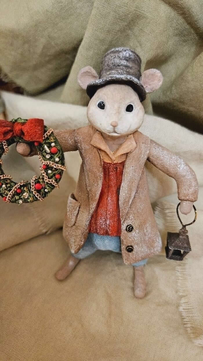 Miniature World: 33 Cotton Wool Sculptures by Katya Celebrating the Magic of Handmade Craft 66 A handcrafted cotton wool mouse ornament stands on soft neutral fabric, dressed in a frosted beige coat and tall top hat, holding a festive wreath in one hand and a tiny lantern in the other, styled in a vintage holiday aesthetic.