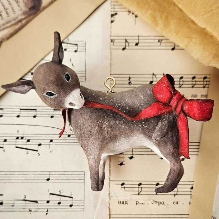 Miniature World: 33 Cotton Wool Sculptures by Katya Celebrating the Magic of Handmade Craft 72 A handcrafted cotton wool reindeer ornament is posed against vintage sheet music, turning its head gently to the side while wearing a long red scarf tied in a dramatic bow, with softly dusted details that give it a wintry, storybook charm.