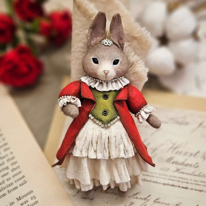 Miniature World: 33 Cotton Wool Sculptures by Katya Celebrating the Magic of Handmade Craft 42 A handcrafted miniature rabbit ornament made from cotton wool wears a rich red coat, olive-green bodice, and layered cream dress with delicate ruffled details, posed against a soft vintage-inspired background.