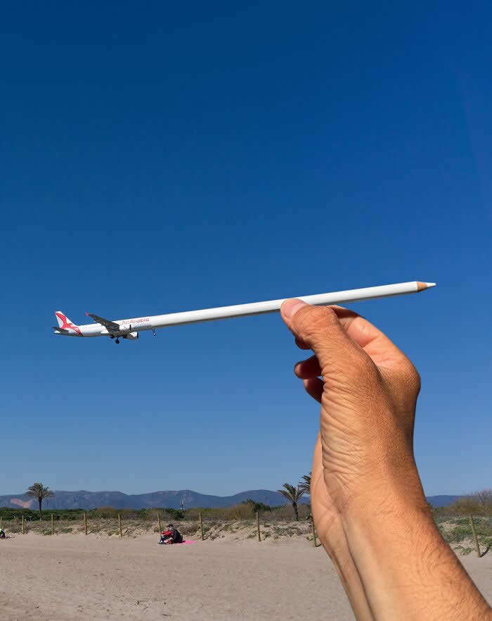 Pure Visual Magic: 35 Mind-Bending Forced Perspective Photos by Hugo Suíssas 52 A hand holds a white pencil in the foreground, perfectly aligned with a plane flying across a clear blue sky so the aircraft appears to be attached to the pencil like it’s being drawn in a playful forced perspective illusion.