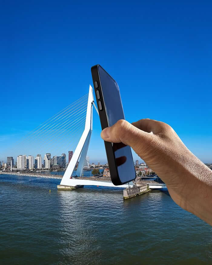 Pure Visual Magic: 35 Mind-Bending Forced Perspective Photos by Hugo Suíssas 53 A hand holds a black smartphone in the foreground, aligned with a white cable-stayed bridge so the bridge’s tall central pylon appears to emerge from the phone like a sleek extension in a playful forced perspective illusion.