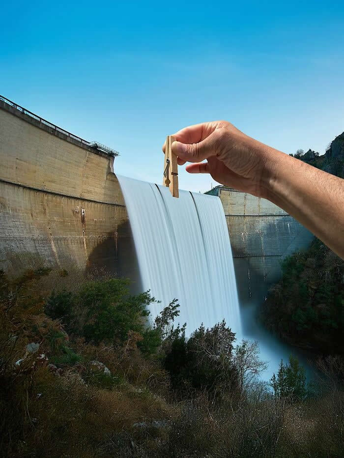 Pure Visual Magic: 35 Mind-Bending Forced Perspective Photos by Hugo Suíssas 54 A hand holds a wooden clothespin above a dam spillway, aligned so the pin appears to clip the rushing sheet of water as it pours over the edge in a playful forced perspective illusion.