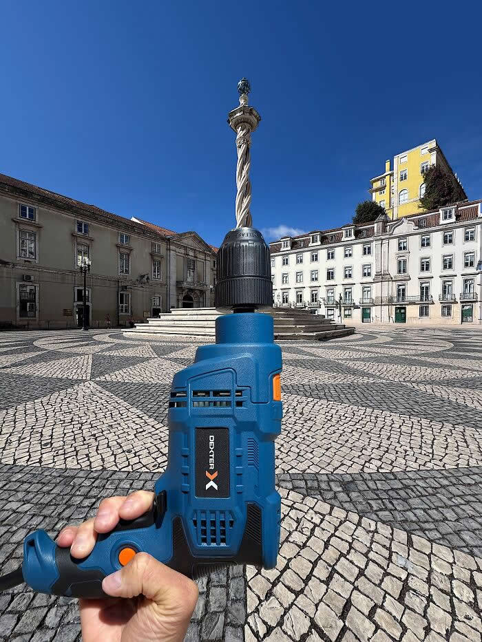 Pure Visual Magic: 35 Mind-Bending Forced Perspective Photos by Hugo Suíssas 55 A hand holds a blue power drill in the foreground, aligned with a tall stone column in a city square so the monument appears to become the drill bit in a playful forced perspective illusion.