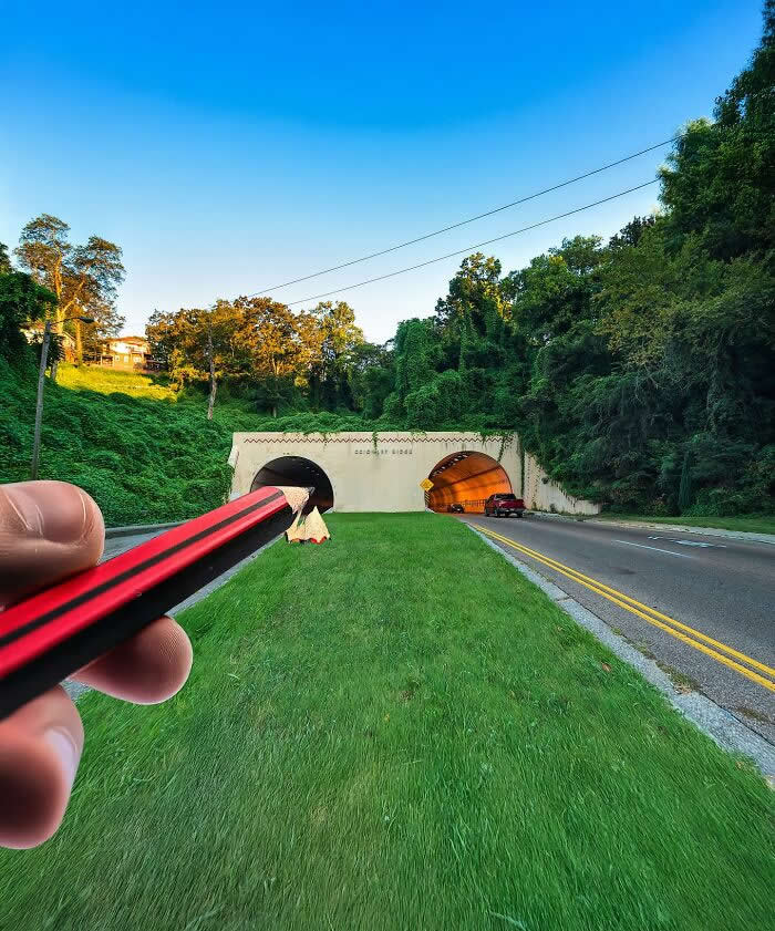 Pure Visual Magic: 35 Mind-Bending Forced Perspective Photos by Hugo Suíssas 67 A hand holds a red pencil in the foreground, aligned with a pair of road tunnels so the pencil appears to slide directly into one tunnel like a sharpened tip in a playful forced perspective illusion.