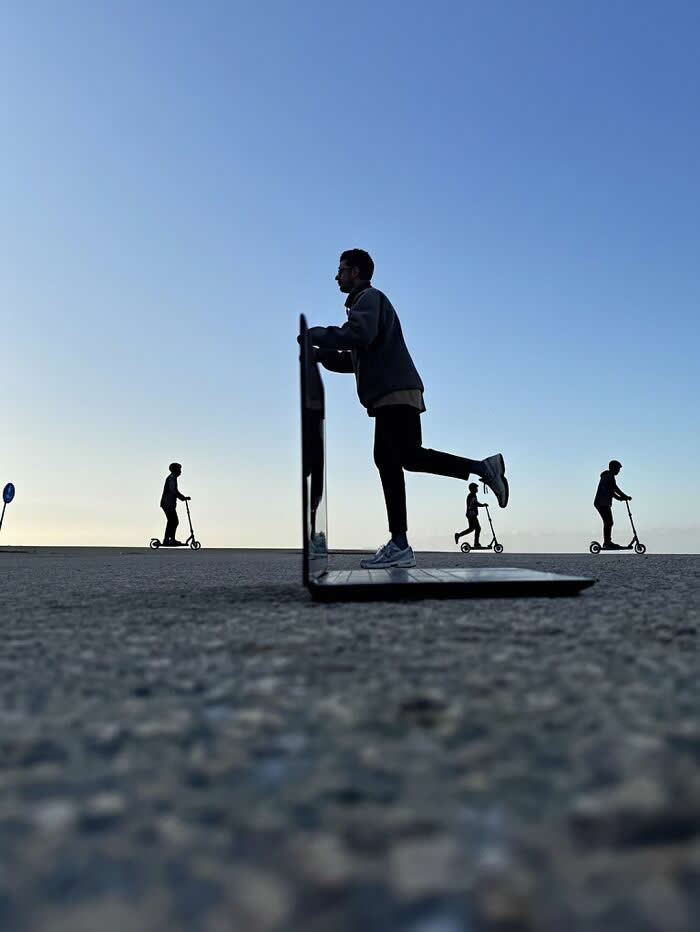 Pure Visual Magic: 35 Mind-Bending Forced Perspective Photos by Hugo Suíssas 70 A person appears to ride a scooter through the screen of an open laptop placed on the ground, while other scooter riders move across the horizon in the background, creating a playful forced perspective illusion.