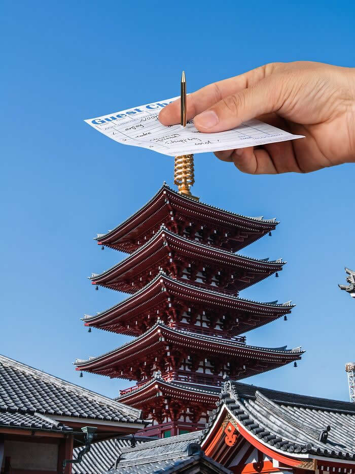 Pure Visual Magic: 35 Mind-Bending Forced Perspective Photos by Hugo Suíssas 71 A hand holds a guest check and pen above a traditional five-story pagoda, aligned so the pen appears to be inserted into the pagoda’s golden spire, creating a playful forced perspective illusion against a clear blue sky.