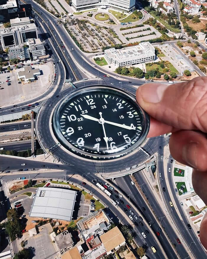 Pure Visual Magic: 35 Mind-Bending Forced Perspective Photos by Hugo Suíssas 72 A hand holds a black wristwatch above an aerial view of a large traffic roundabout, aligning the watch face with the circular road so the roundabout appears to become part of the watch in a playful forced perspective illusion.