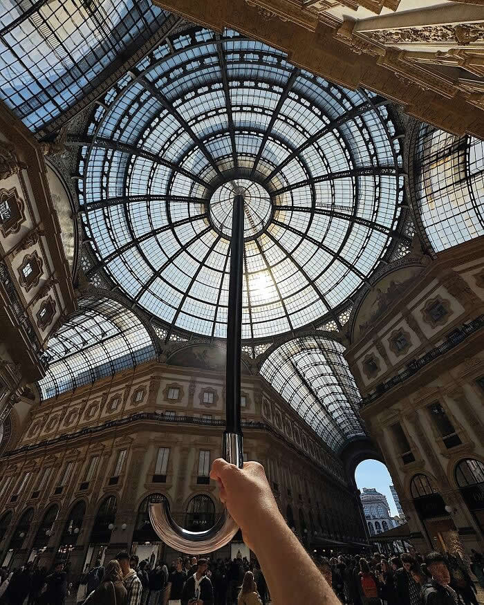 Pure Visual Magic: 35 Mind-Bending Forced Perspective Photos by Hugo Suíssas 42 Inside a grand glass-roofed arcade, a hand holds a closed umbrella upward, perfectly aligned with the circular dome so it looks like the umbrella is supporting the entire ceiling in a dramatic forced perspective composition.