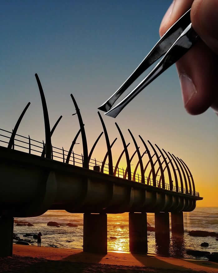 Pure Visual Magic: 35 Mind-Bending Forced Perspective Photos by Hugo Suíssas 43 A hand holds a pair of tweezers above a seaside pier at sunset, aligned so the tweezers appear to pluck one of the curved metal beams from the structure in a clever forced perspective illusion.
