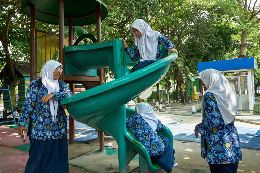 The Art of Perfect Timing: 34 Clever Street Photos by Emiliano Cuadrado That Turn Ordinary Scenes Into Visual Surprises 50 Children in matching school uniforms play on a green spiral slide, appearing at different points to create a playful, perfectly timed street photography composition surrounded by lush park greenery.