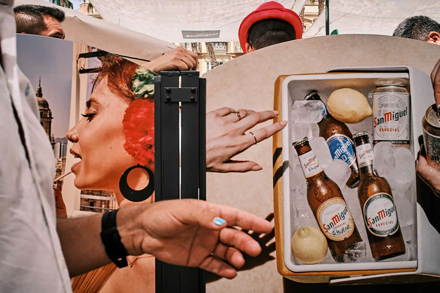 The Art of Perfect Timing: 34 Clever Street Photos by Emiliano Cuadrado That Turn Ordinary Scenes Into Visual Surprises 45 Crowded street scene with overlapping advertising displays, hands reaching across the frame, and pedestrians partially obscured, creating a colorful, layered composition filled with visual illusions and perfectly timed interactions.